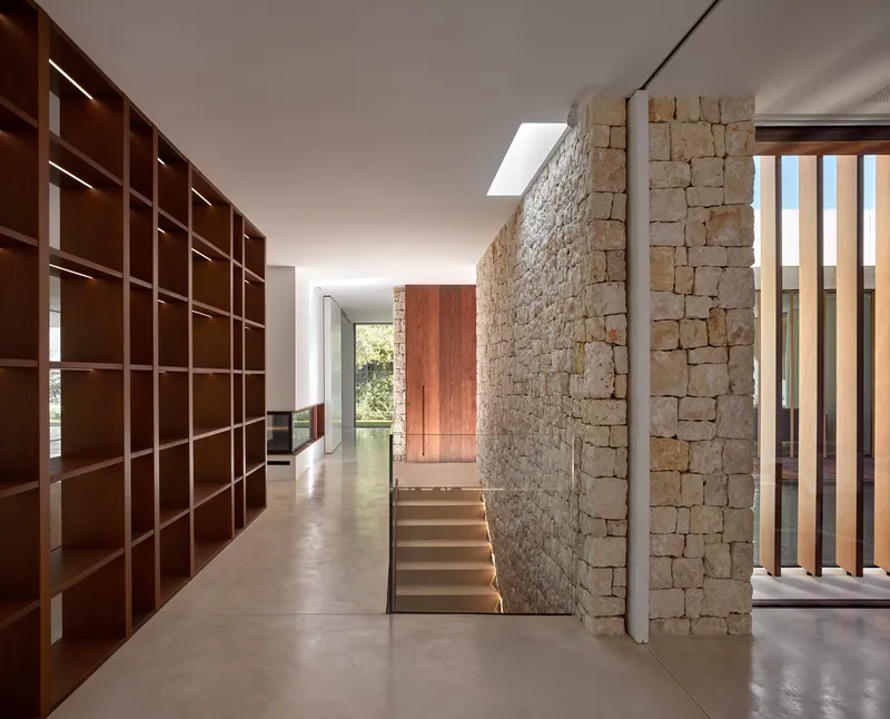 Stone wall enclosing the stairwell with walnut shelving and skylight above polished concrete floors