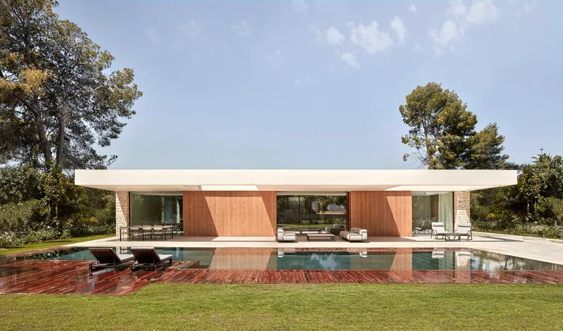 Garden facade with flat roof and wood-clad volumes flanking a covered terrace overlooking the swimming pool