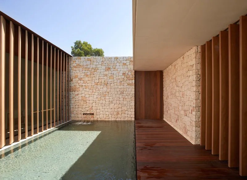 Covered walkway with timber decking alongside the pool edge and stone block walls under midday sun