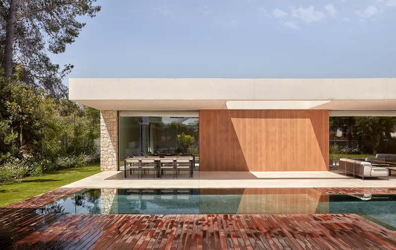 Poolside view showing timber deck, stone wall, and white cantilevered roof with dining terrace below