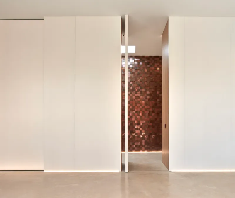 Pivoting door revealing terracotta tile wall through narrow opening with concealed lighting