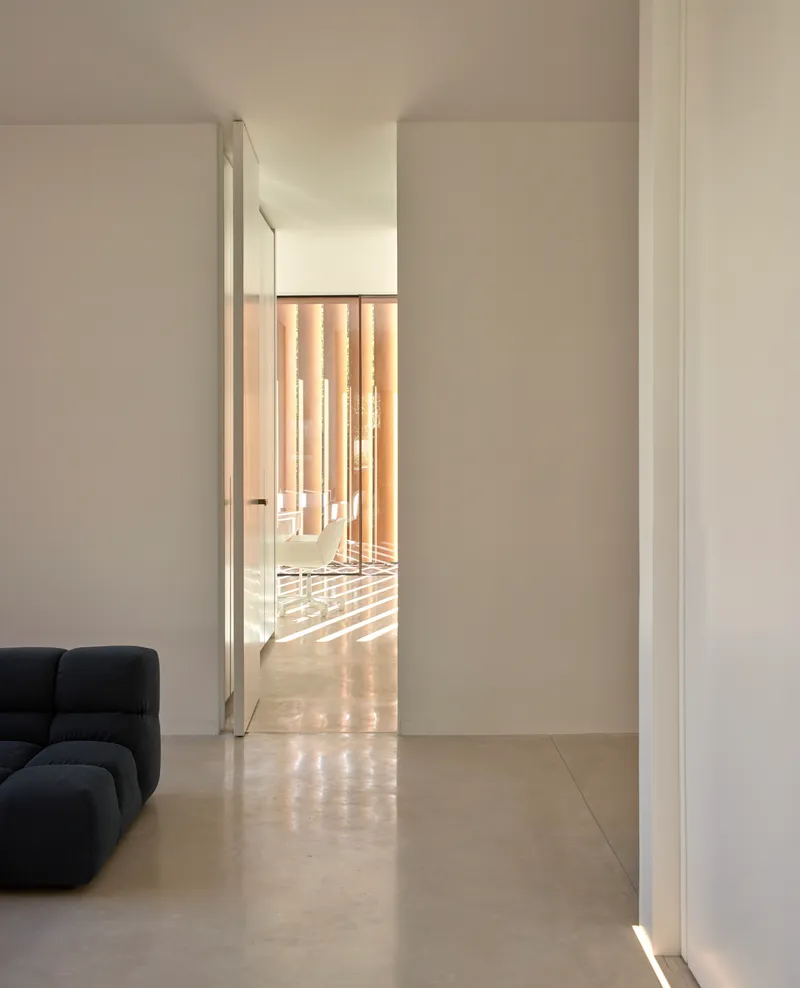 View through doorway to sunlit room with vertical wood slat screen casting shadows