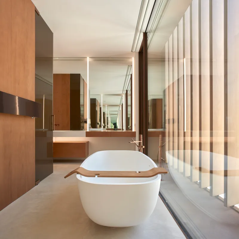 Bathroom with freestanding white tub beside vertical wood slat screen filtering daylight