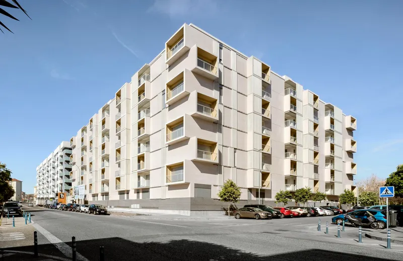 Street corner view of the white paneled residential block with recessed balconies under clear blue sky