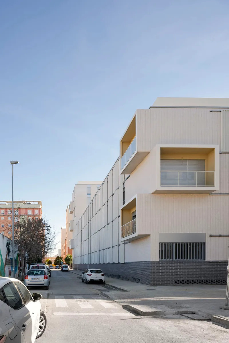 Corner view showing projecting balconies with yellow reveals and the metal panel facade in afternoon light