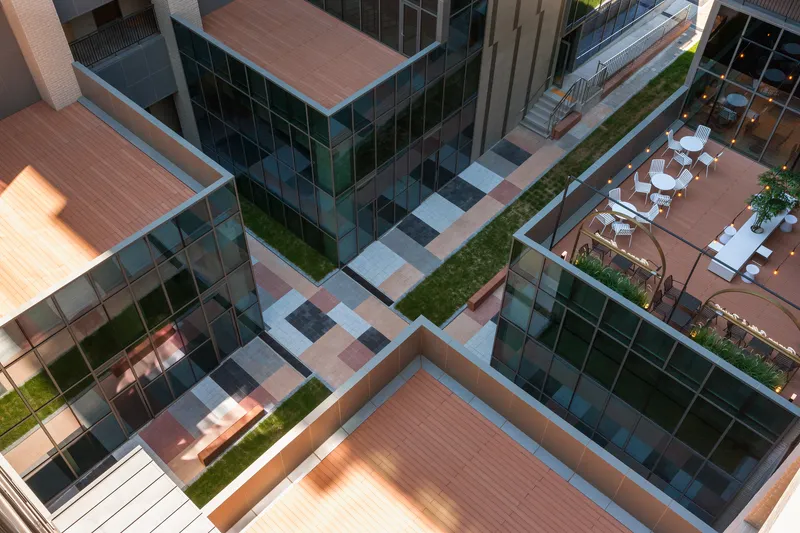 Aerial view of the central courtyard with paved terraces, planted strips, and rooftop seating areas in afternoon light