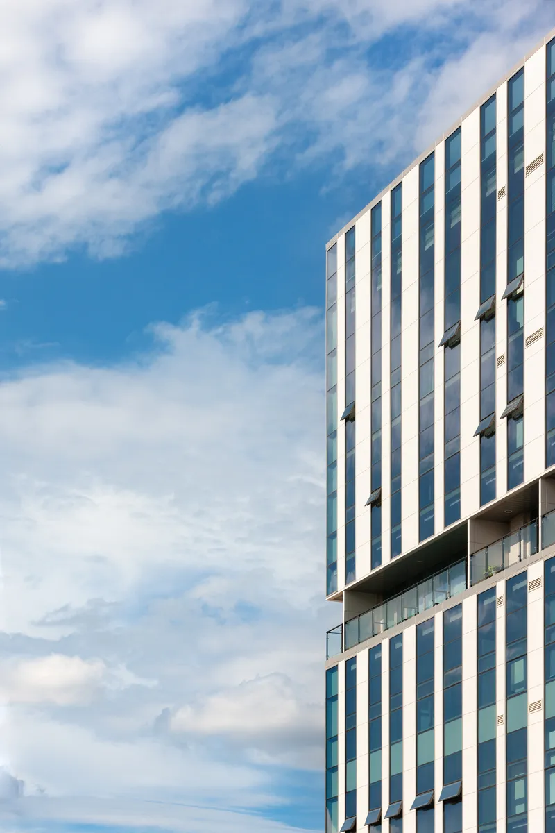 Vertical striped facade with white and grey panels rising against a blue sky with scattered clouds
