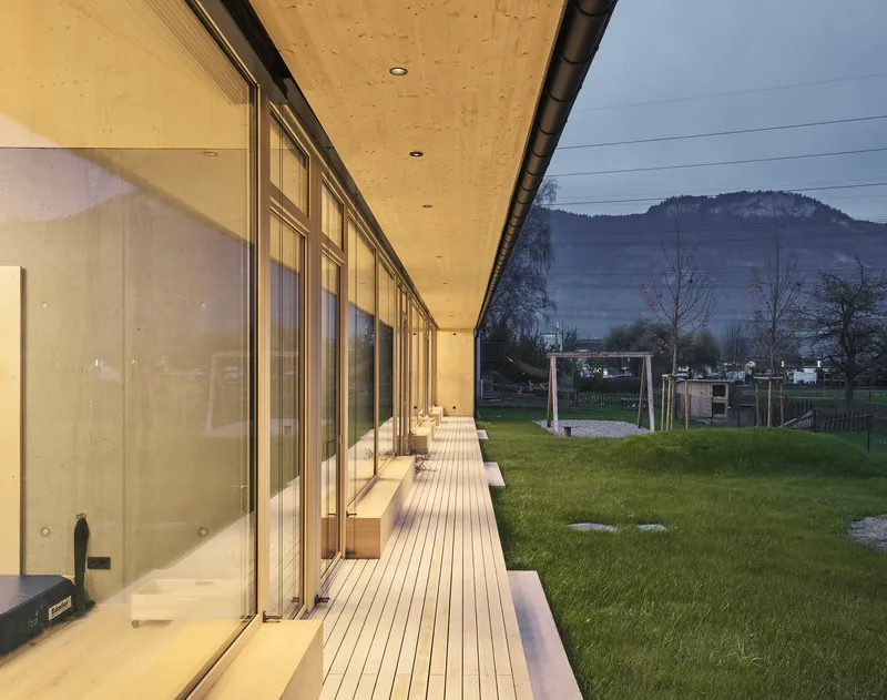 Long exterior deck alongside glazed facade with hills visible beyond the grassy field
