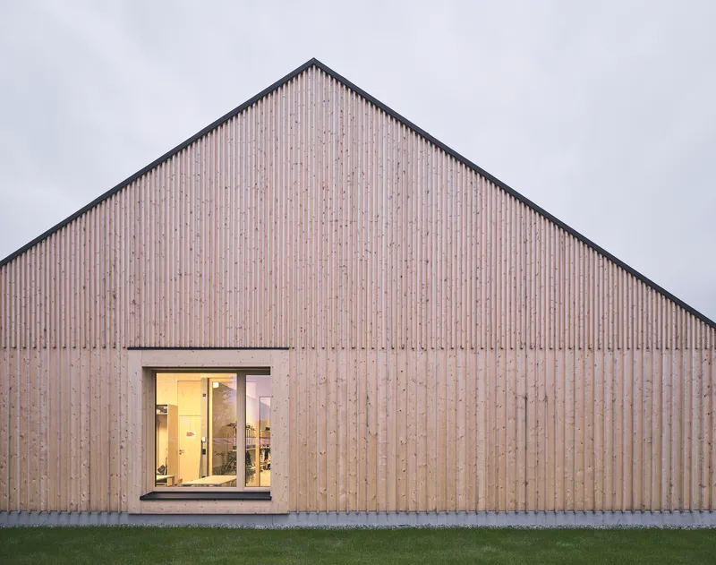 Vertical timber slat gable facade with single punched window opening at twilight