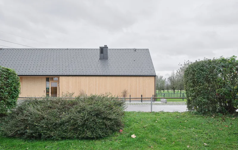 Gable end elevation with vertical timber cladding and small entrance portal beside low shrubs