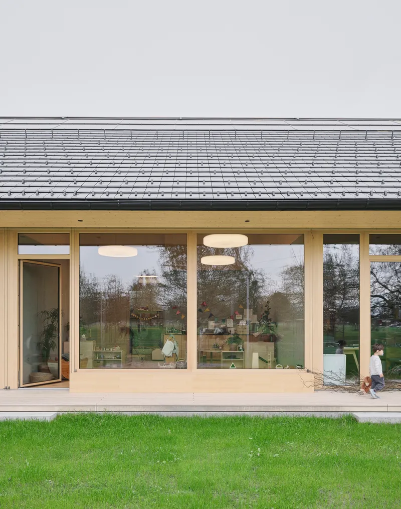 Glazed facade with timber frames beneath deep eave overhang and grey tile roof with child walking