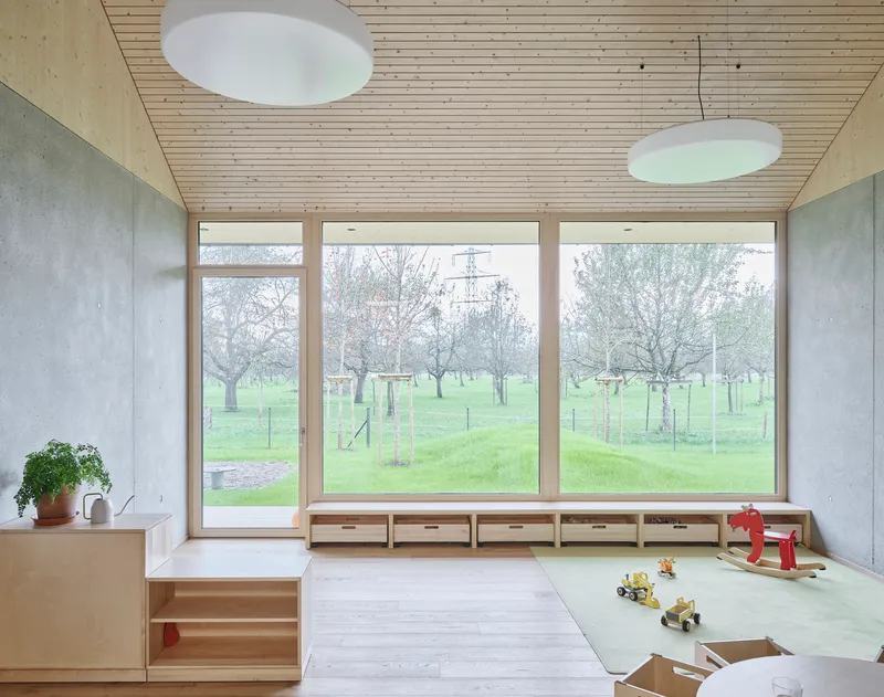 Interior room with timber ceiling, concrete walls, low built-in storage and windows overlooking park