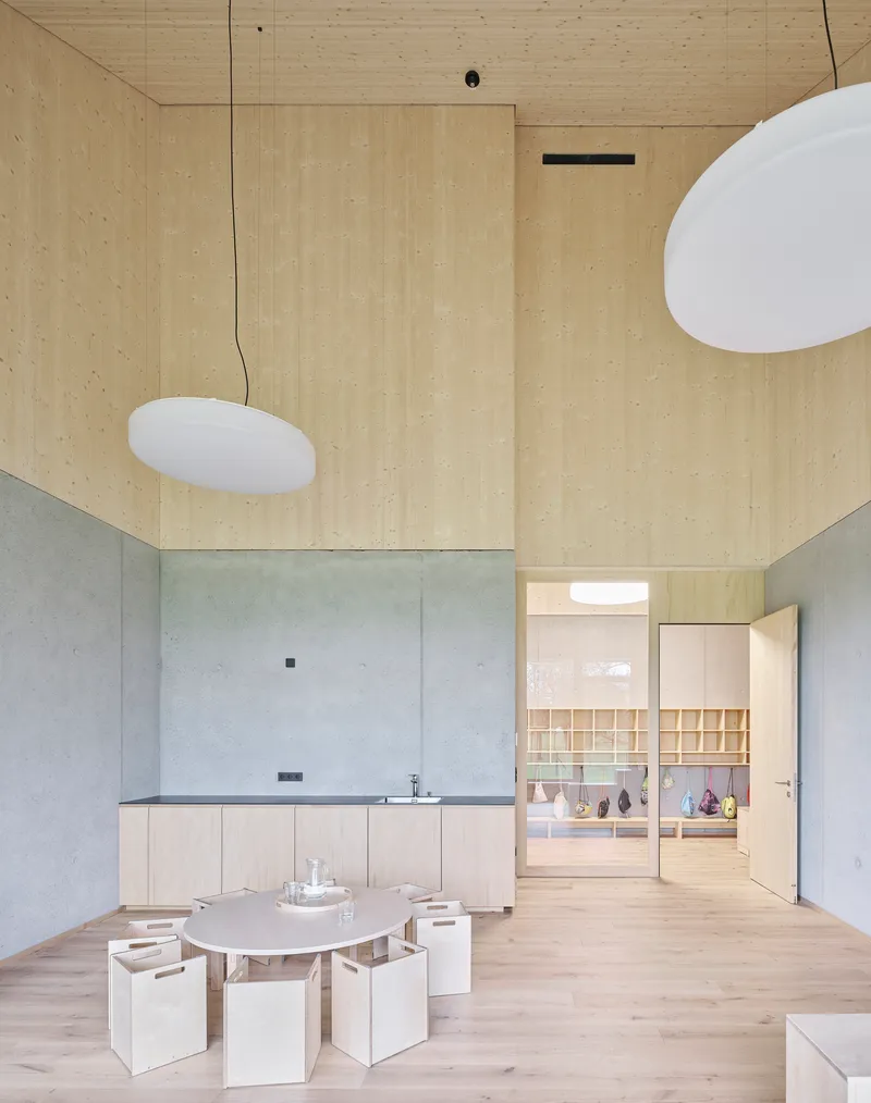 Double-height interior with plywood walls and ceiling above a concrete base and low seating around a table