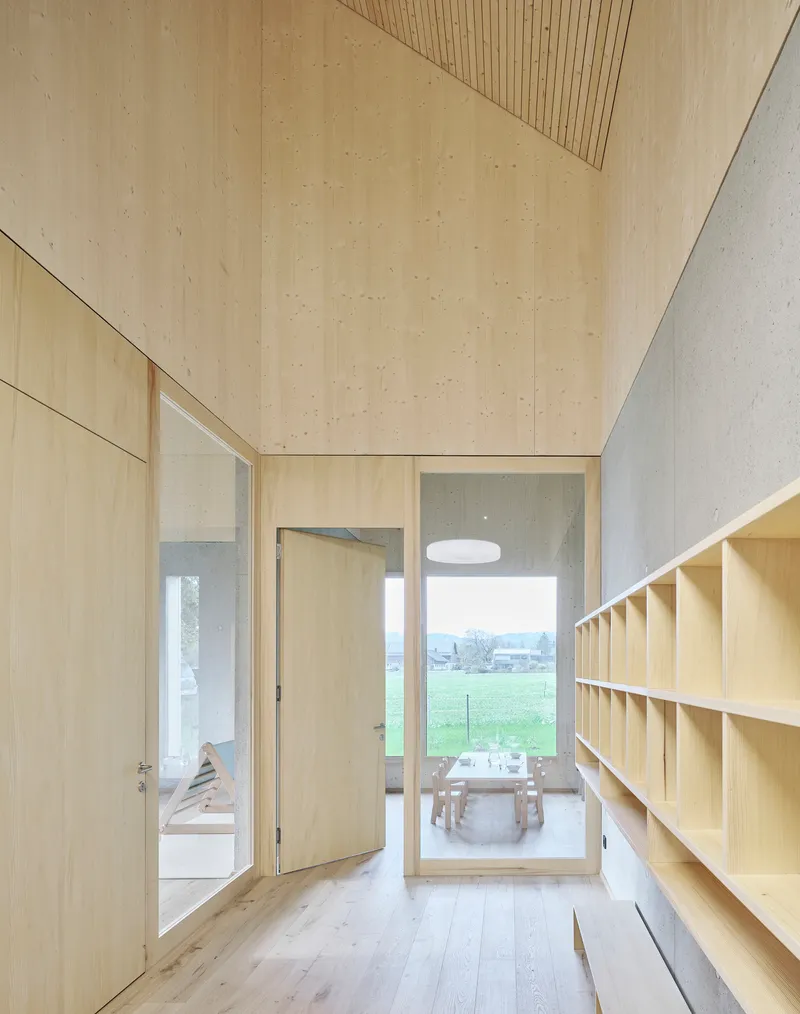 Corridor with plywood walls and slatted ceiling looking through open doors to a dining area beyond the orchard