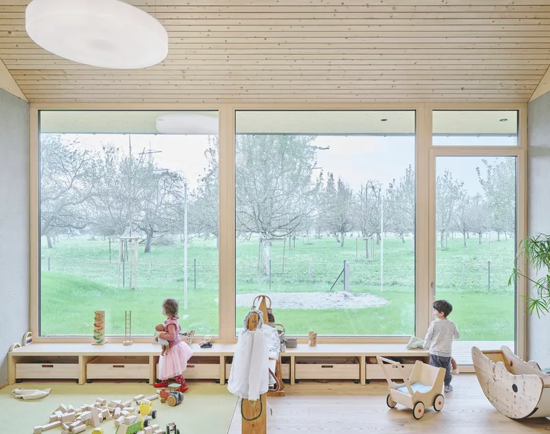 Children playing in a room with floor-to-ceiling windows overlooking the orchard on a misty morning