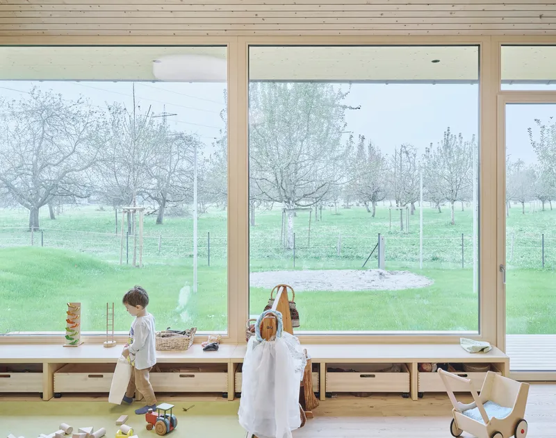 Two children at the window bench with wooden toys looking out to the fenced pasture and trees