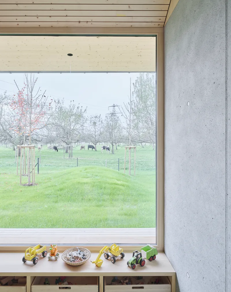 Corner window detail with toy tractors on the sill and cattle grazing beyond the young orchard