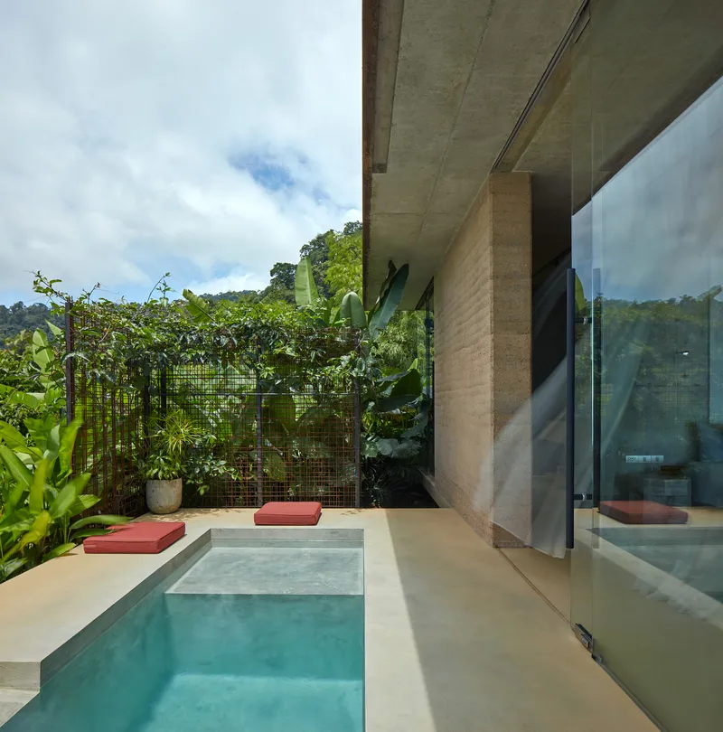 Courtyard pool with red cushioned seating ledges and wire mesh green wall with tropical plants