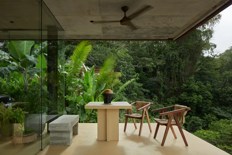Covered dining terrace with exposed concrete ceiling and banana plants framing forested view