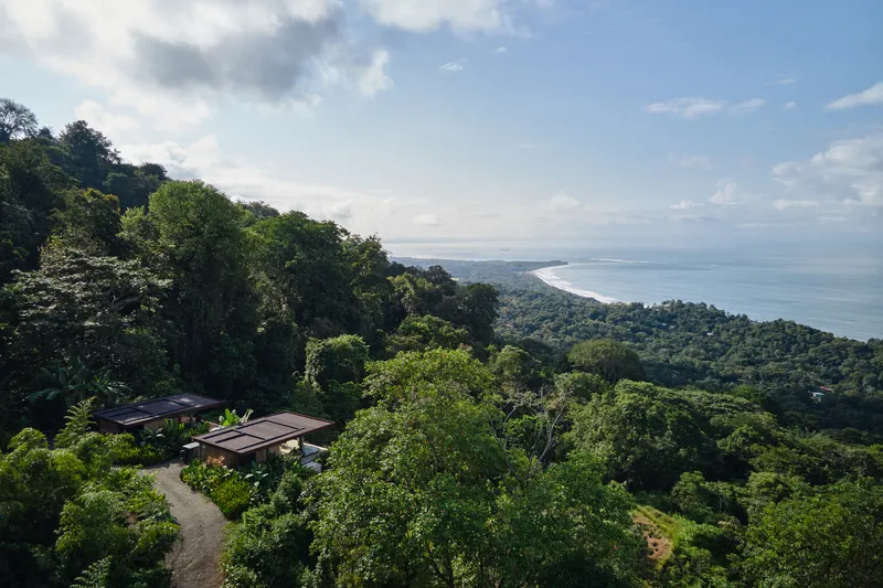 Elevated view of the compound nestled into the hillside with coastline visible beyond forested slopes
