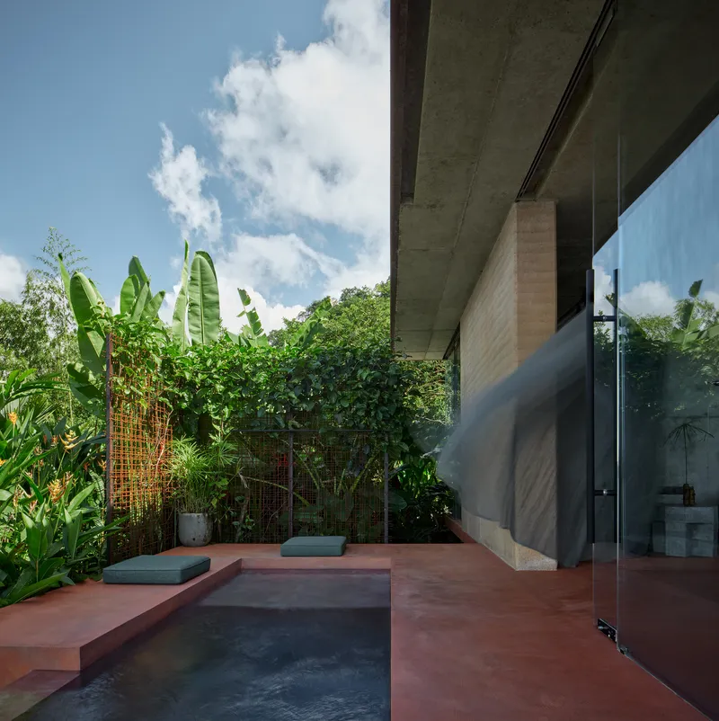 Red-tinted terrace with plunge pool bordered by banana plants and tropical foliage under bright sun