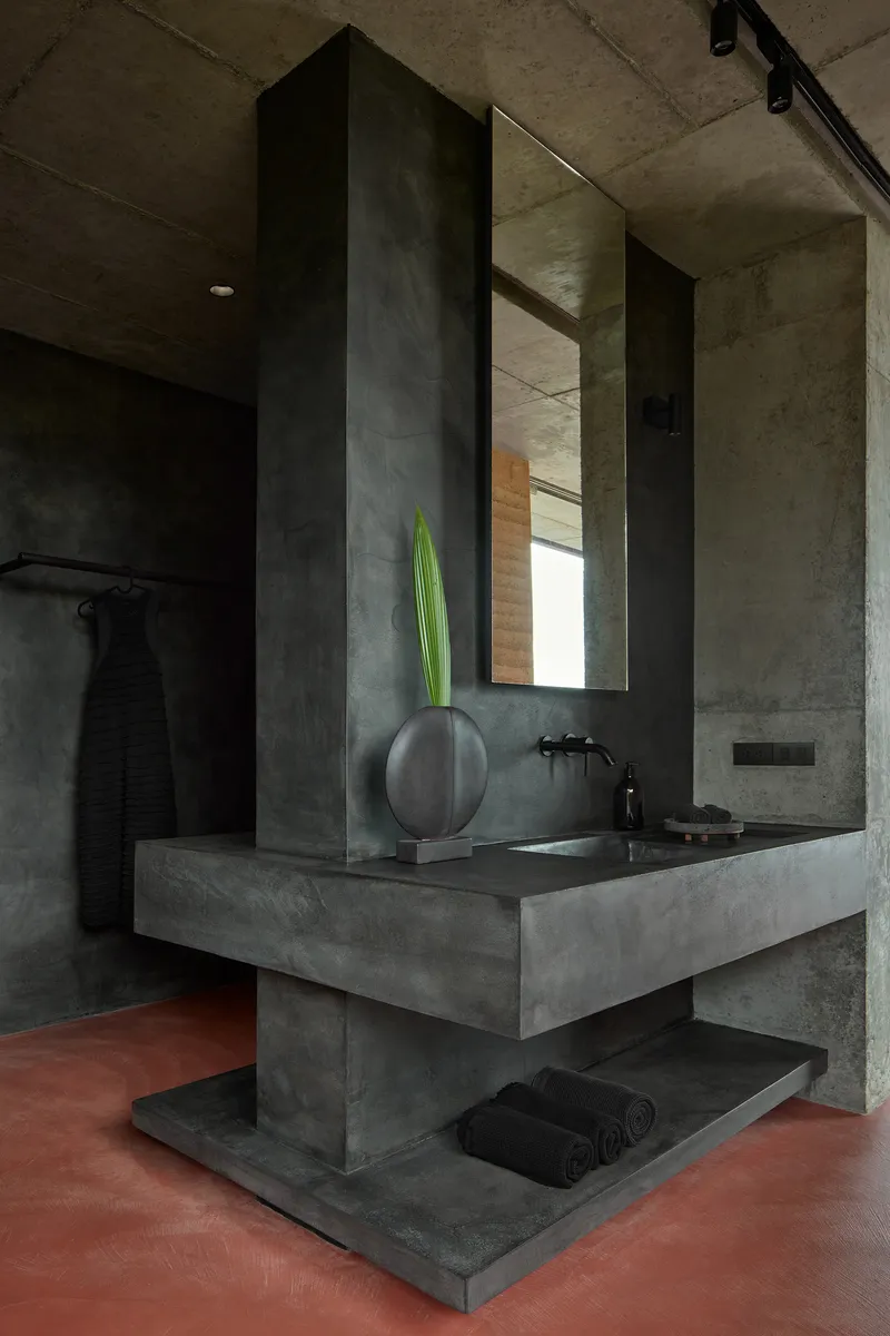 Monolithic concrete vanity with cantilevered sink basin and tall mirror over red oxide floor