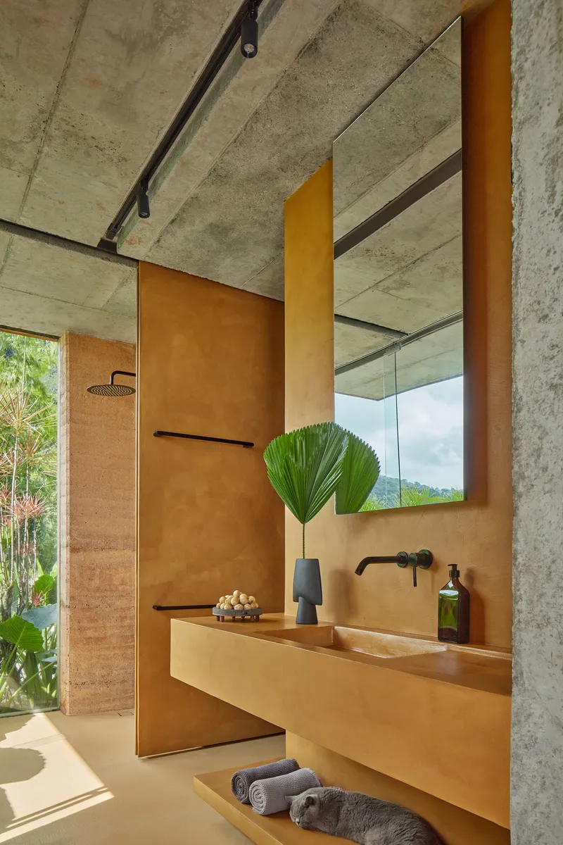 Bathroom vanity with integrated sink in ochre plaster beneath an exposed concrete ceiling and mirrored cabinet