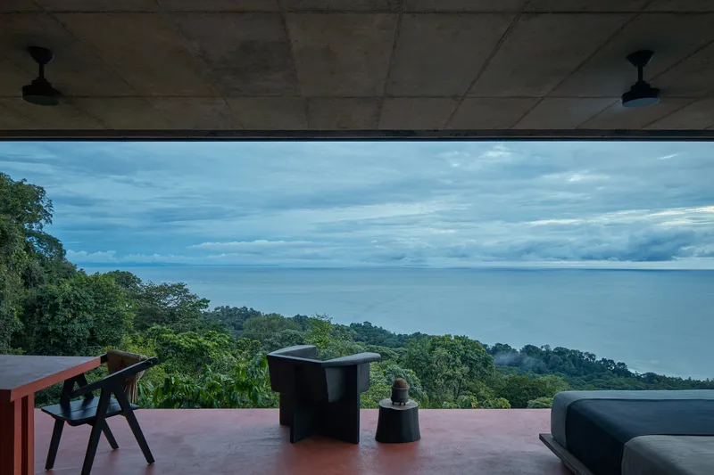 Covered terrace with exposed concrete soffit and ceiling fans overlooking forested coastline and ocean