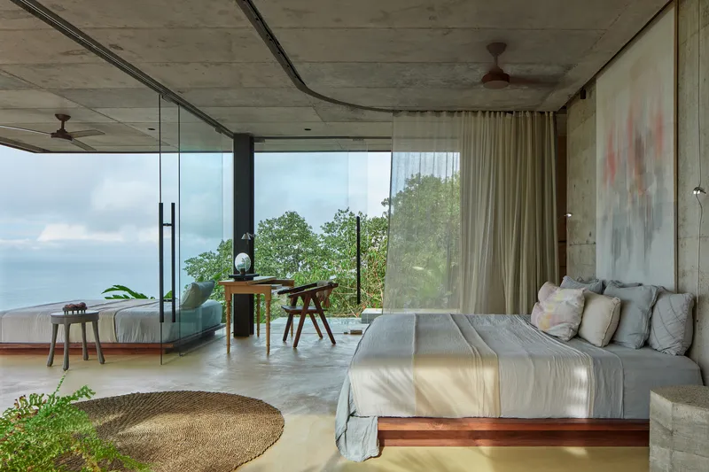 Interior view of bedroom with concrete walls and glass corners opening to ocean vista