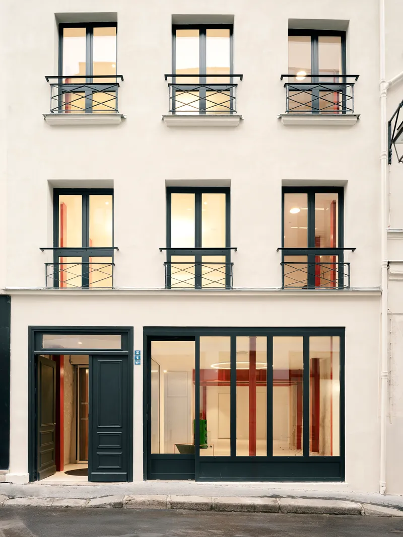 Street facade with black-framed windows, metal railings, and illuminated ground floor glazing at dusk