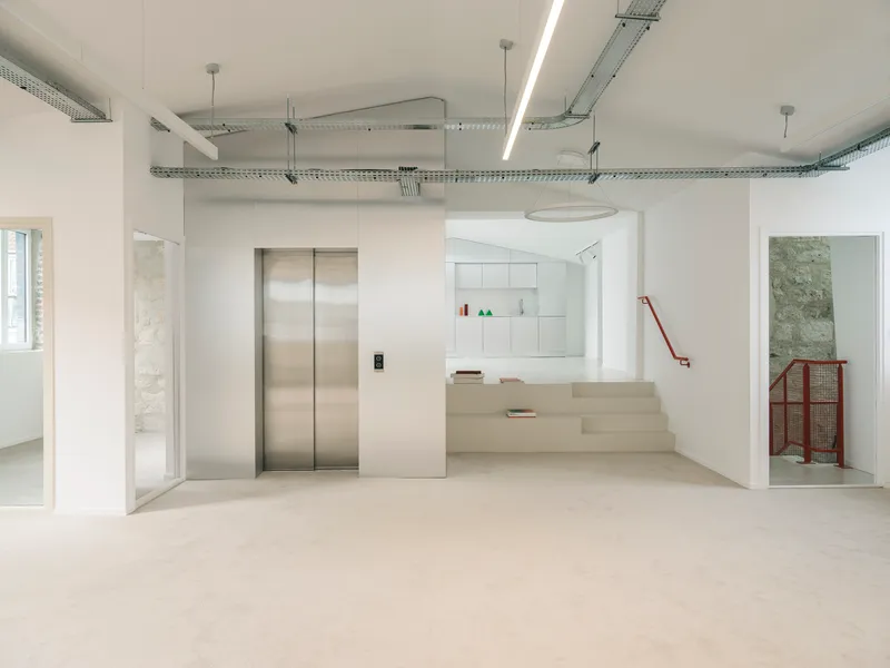 Reception area with stainless steel elevator doors, integrated stair platform, and exposed ductwork above