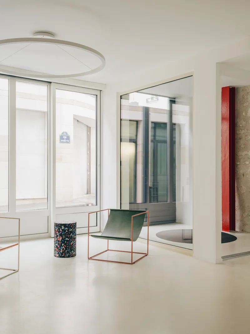 White interior with brass-framed seating and terrazzo planter beneath a circular ceiling fixture
