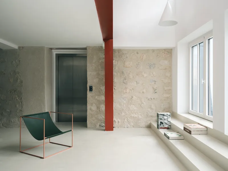 Room with textured limestone walls, a red steel column, and a metal sling chair beside a window