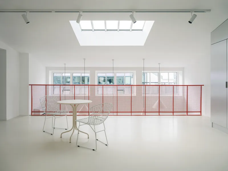 Upper level with red mesh railing and central skylight illuminating the white interior space