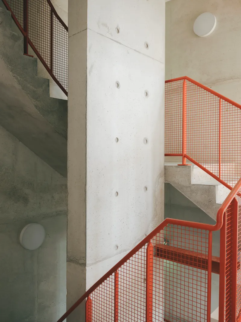 Concrete staircase with orange mesh railings winding around a cylindrical column with circular apertures