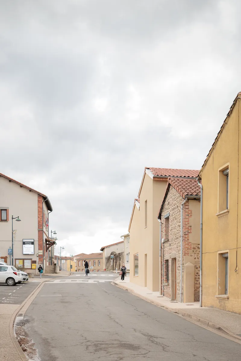 Street view showing mix of new cream-colored plaster and exposed brick facades under overcast sky
