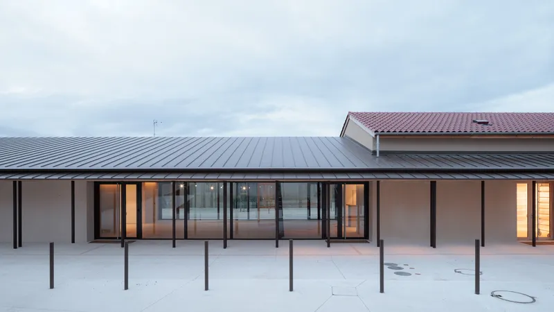Long pavilion with standing seam metal roof and glazed facade with steel columns at dusk