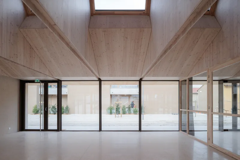 Interior space with exposed timber ceiling beams and full-height glazing overlooking an exterior courtyard