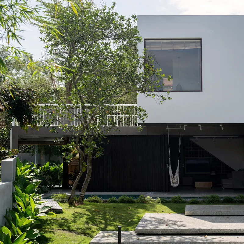 Ground floor terrace with hammock and lawn pathway leading to dark timber facade below white upper volume