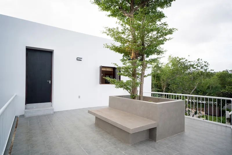 Rooftop terrace with concrete bench planter containing tree and metal railing under overcast sky