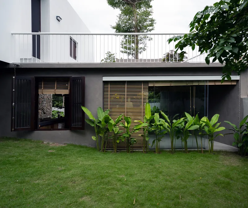 Garden facade with dark concrete wall, timber louvered screen, and banana plants beneath white upper terrace