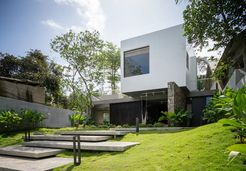 Garden view with wide terrazzo steps ascending through lawn toward the white cubic volume and preserved tree
