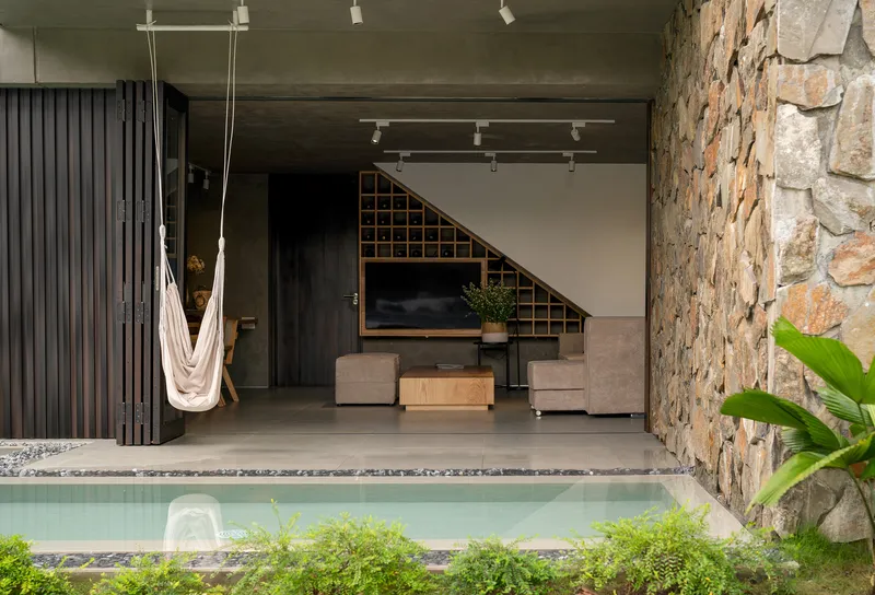 Poolside living area with suspended hammock and irregular stone clad wall beside the water