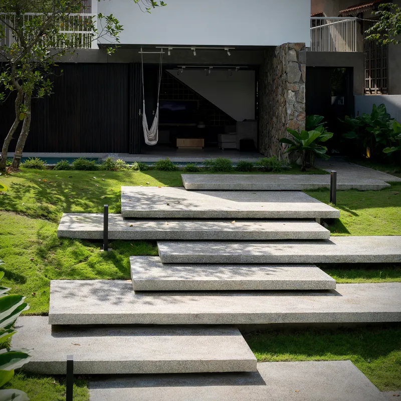 Cascading terrazzo steps through lawn leading to the covered terrace with stone column in dappled sunlight