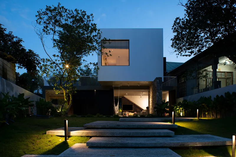 Rear facade with cantilevered white volume and illuminated glazed ground floor at dusk