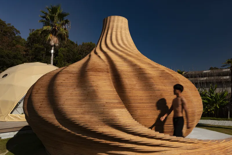 Laminated timber shell with spiral ribs and a person walking through afternoon shadows