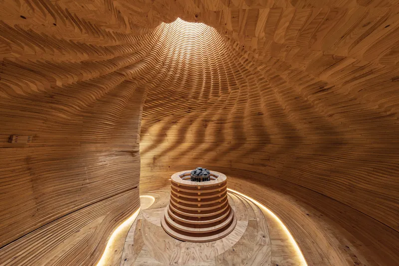 Interior of timber dome with circular oculus casting light onto central sauna drum below