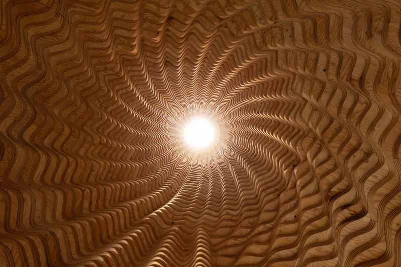 Upward view through ribbed timber oculus with sunlight filtering through the central opening