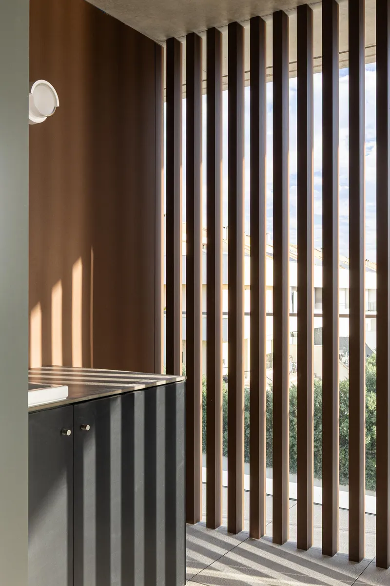 Vertical timber slat screen separating an interior space with sunlight casting shadows on the floor