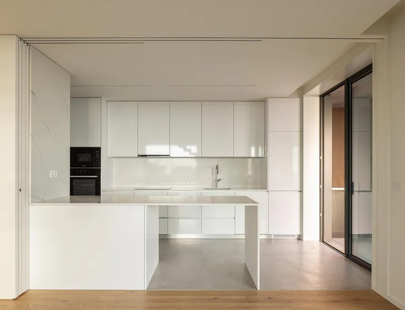 White kitchen with integrated island and marble backsplash opening onto timber flooring in soft natural light